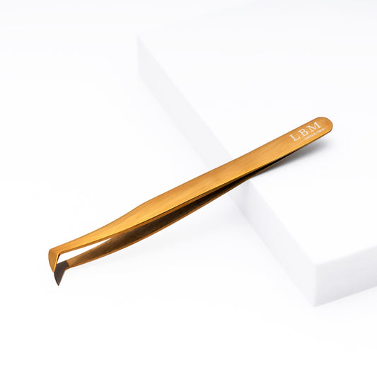 Gold-colored tweezer with 'LBM' branding on a white background
