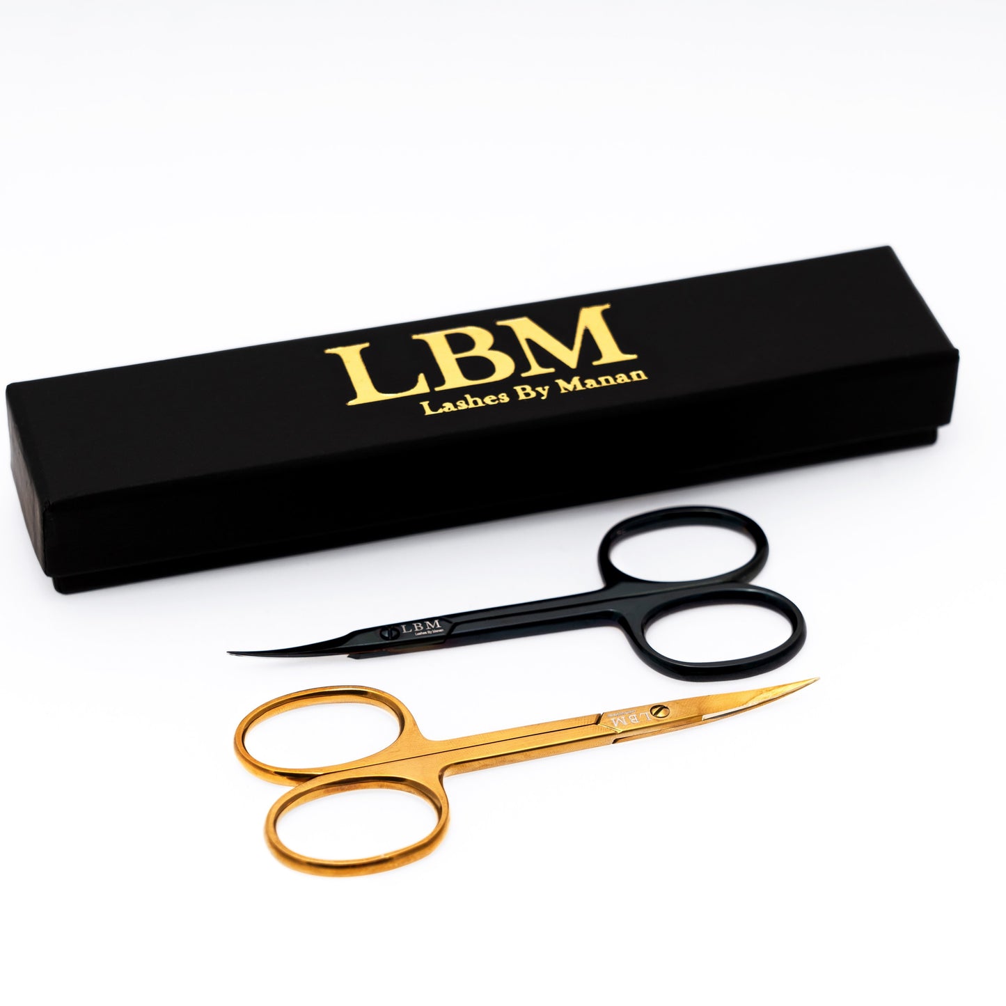 Pair of gold scissors with black handles next to a black box labeled 'Lashes By Manan' on a white background.
