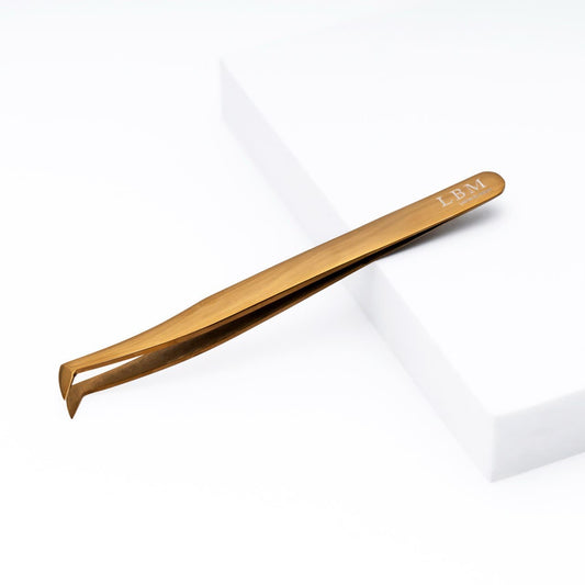 Gold-colored tweezer with 'LBM' branding on a white background